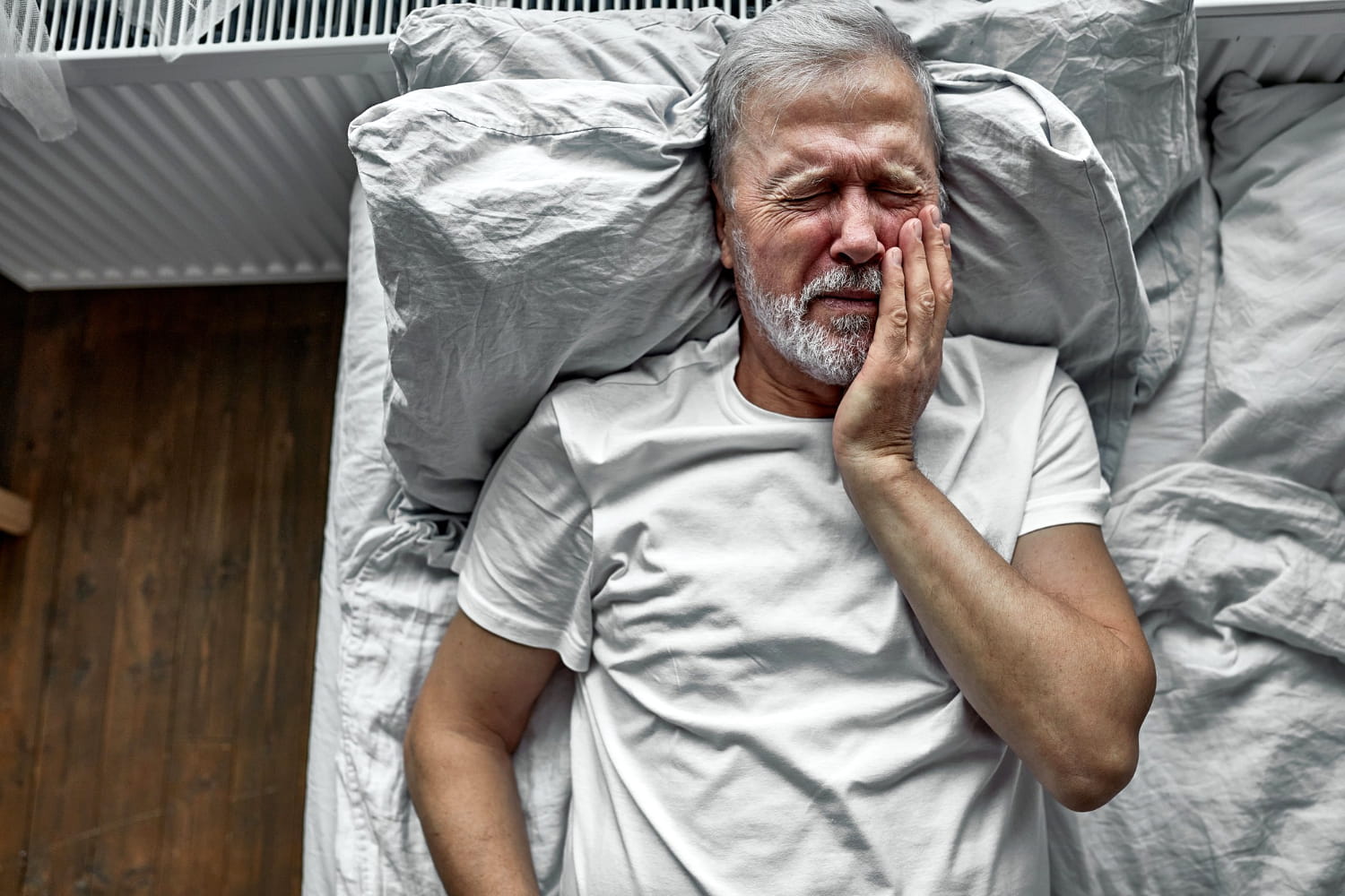 Older man laying in bed with tooth pain