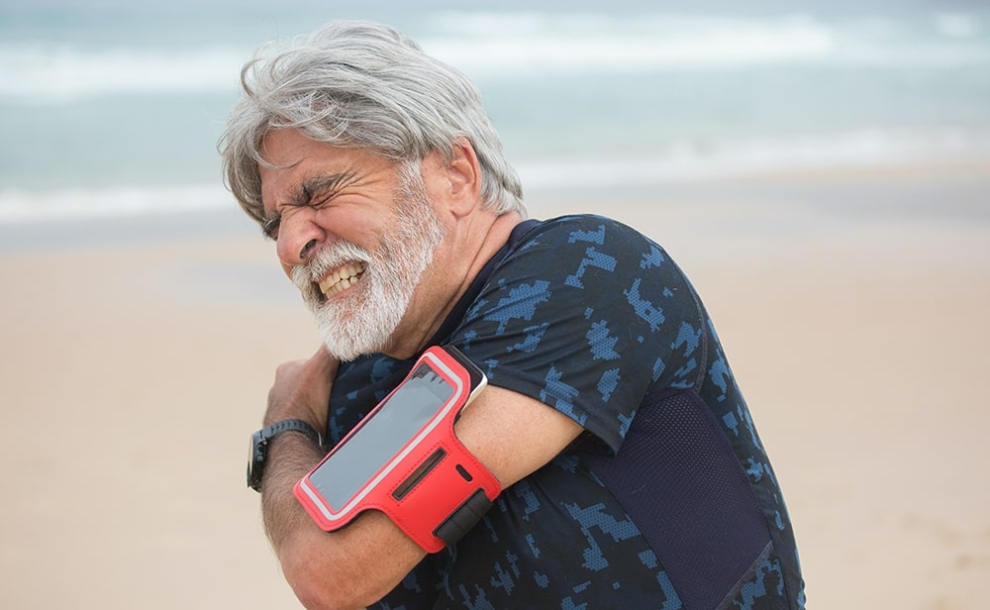 Man on beach with pain in the shoulder